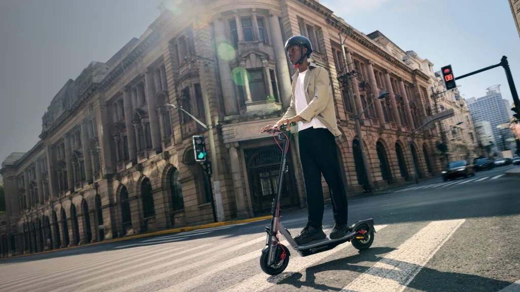 Trottinette électrique Ninebot E3 E en mouvement dans une rue urbaine, conducteur élégant et dynamique, illustration de la mobilité moderne et pratique en milieu citadin